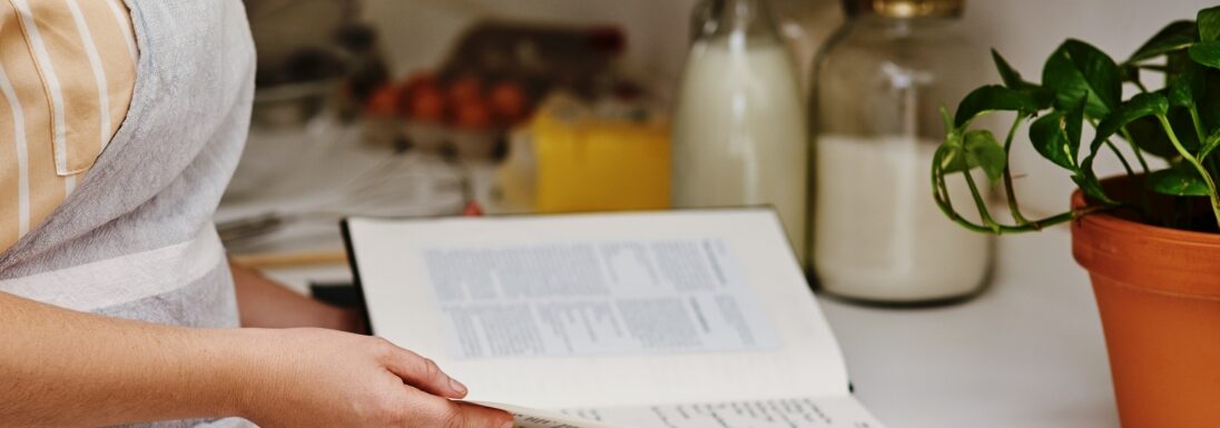 Woman opening a cookbook in her kitchen looking for a recipe