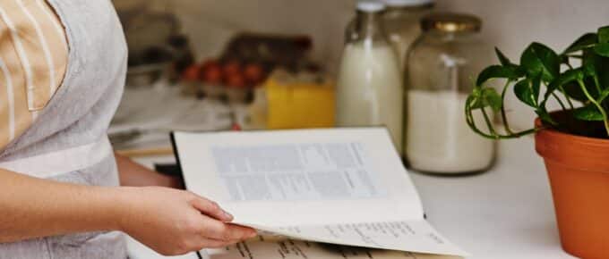 Woman opening a cookbook in her kitchen looking for a recipe