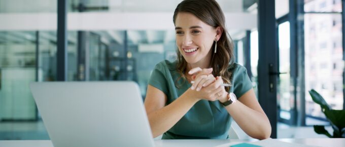 Woman designer speaking on a laptop with notebook of notes laid out on desk.