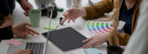 Laptop, Ipad, color samples on desk as people discuss