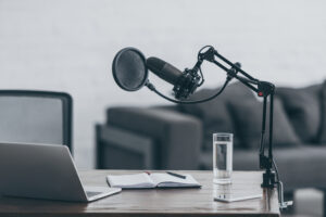 Postcast set up, microphone, laptop, notebook, pen, glass of water, on a table
