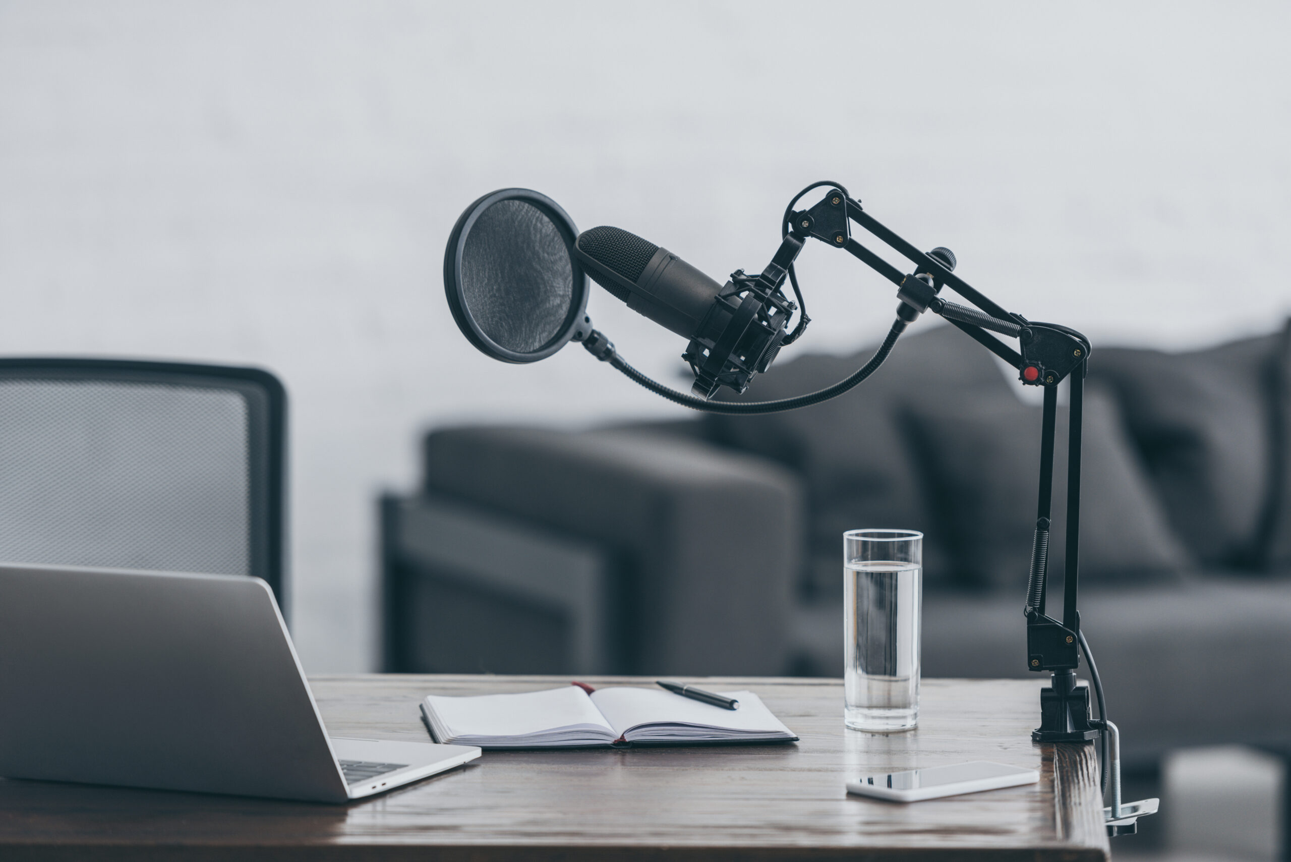 Postcast set up, microphone, laptop, notebook, pen, glass of water, on a table